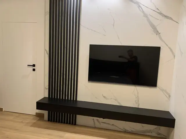 Czarna szafka RTV z lamelami na ścianie telewizyjnej